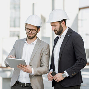 Zwei Männer mit Bauhelm schauen auf Tablet